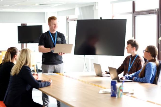 Four colleagues facing a man holding a laptop