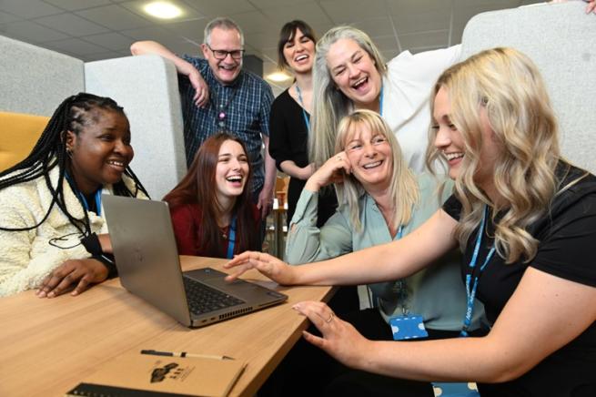 7 colleagues looking at a laptop and smiling