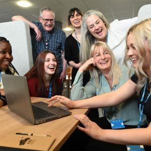 7 colleagues looking at a laptop and smiling